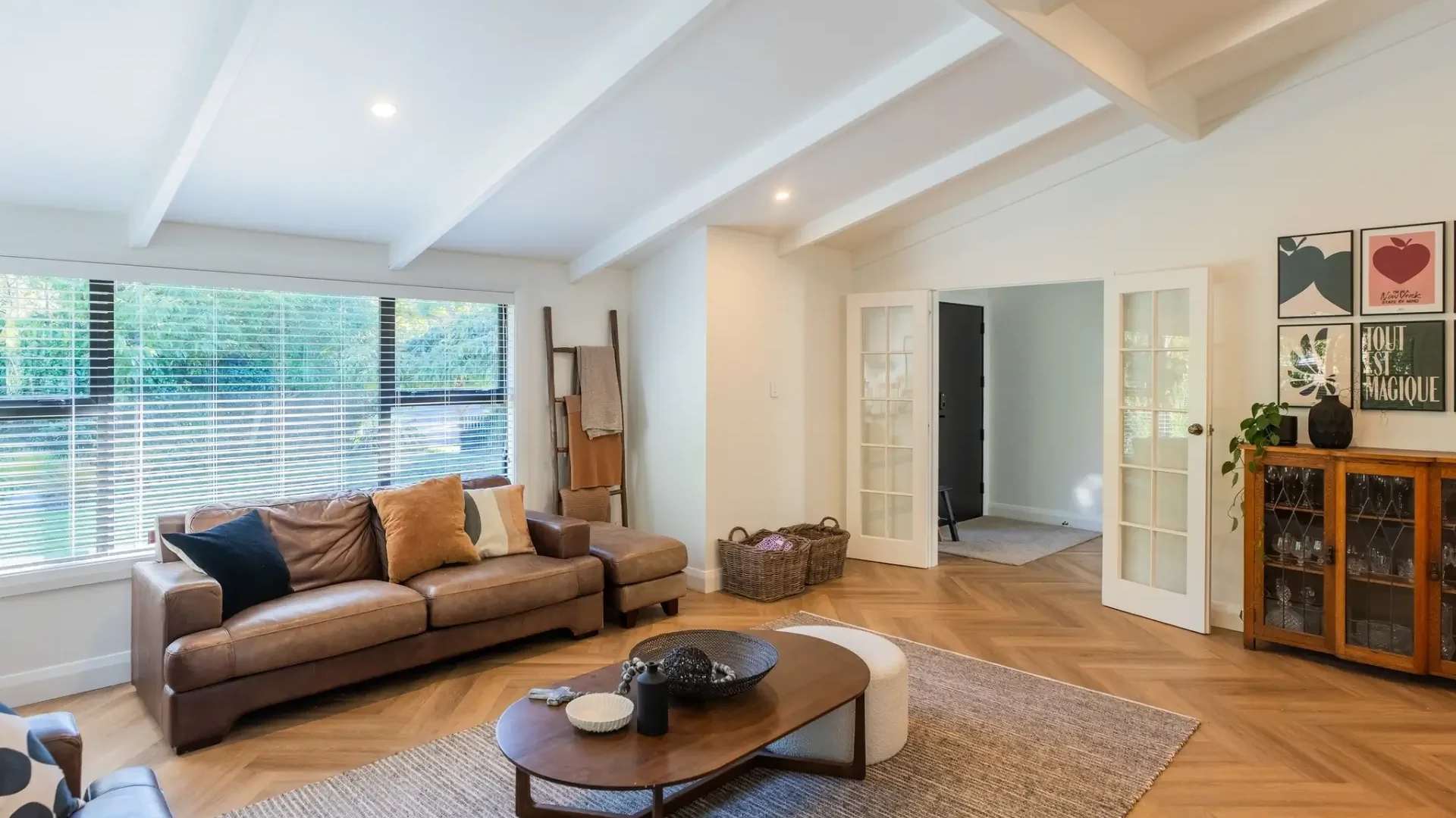 Renovated living room with herringbone timber floors, a leather sofa and a white exposed-beam ceiling